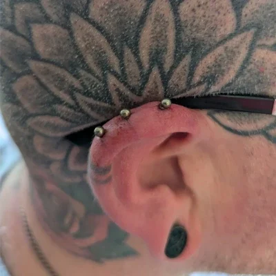 Tripe Helix Ear Piercing Side view of a heavily tattooed man's head, showing a triple helix ear piercing.